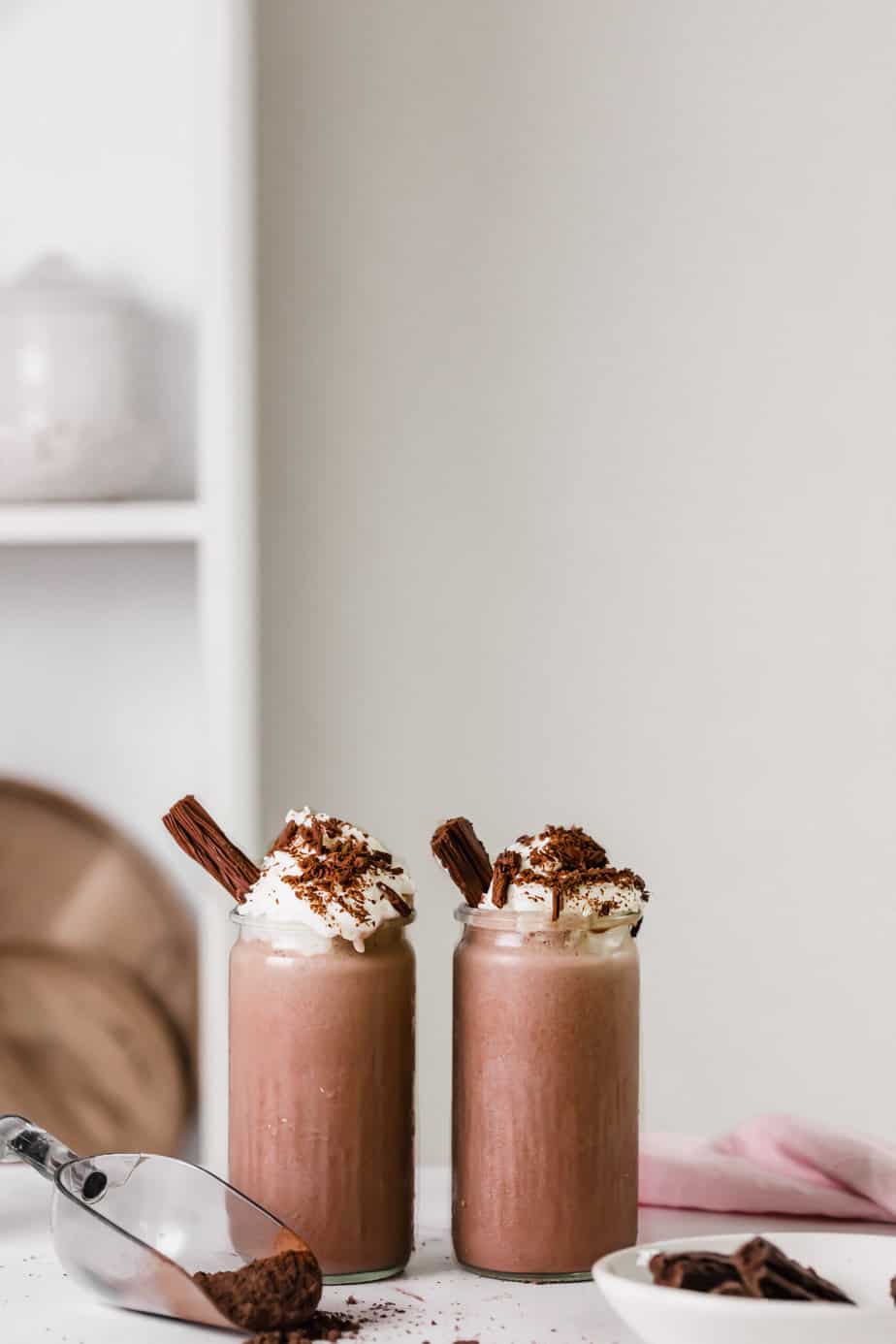 Two chocolate milkshakes in serving glasses with whipped cream and chocolate
