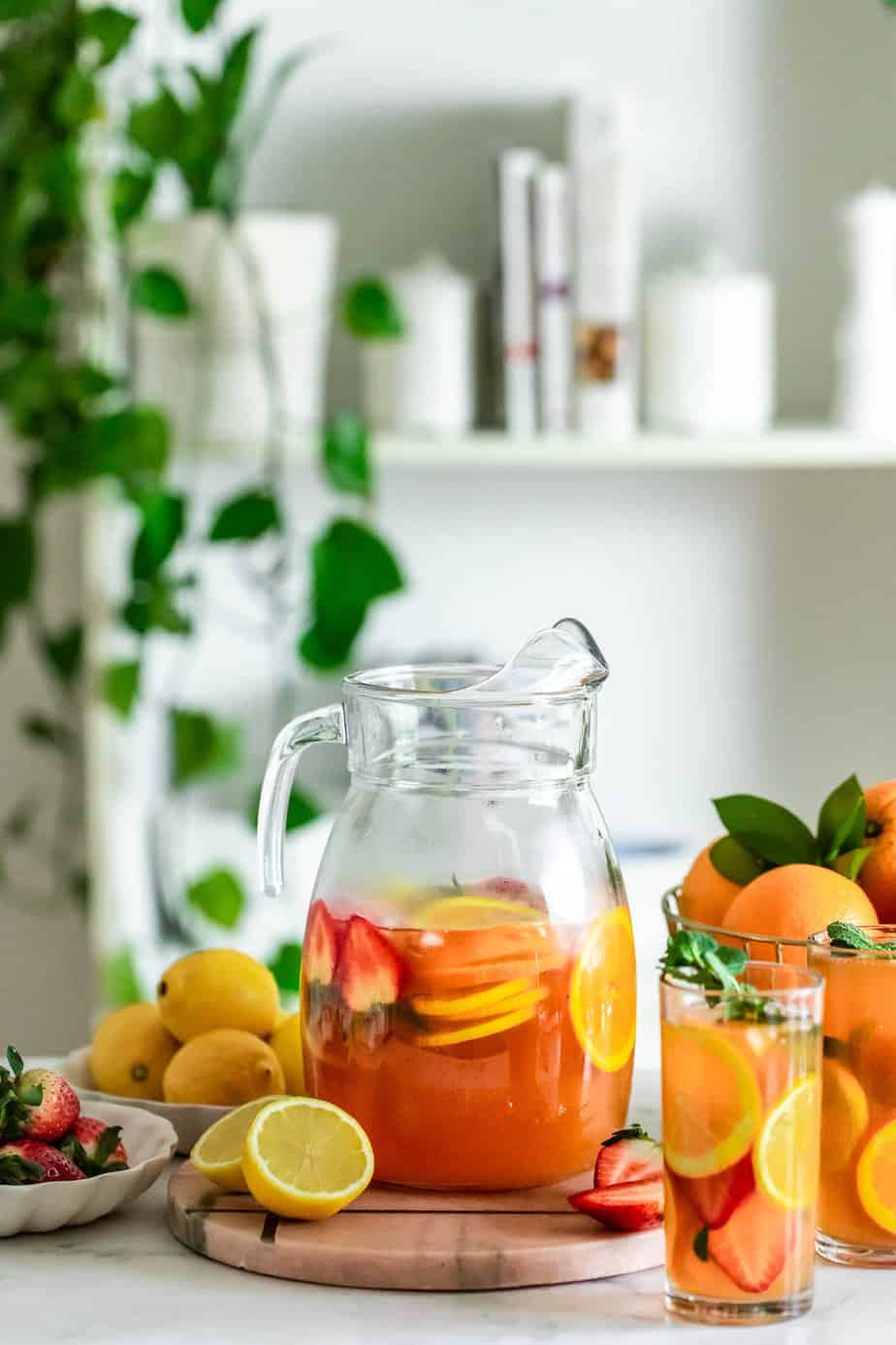 A jug and glasses full of peach green tea surrounded by fresh fruit.