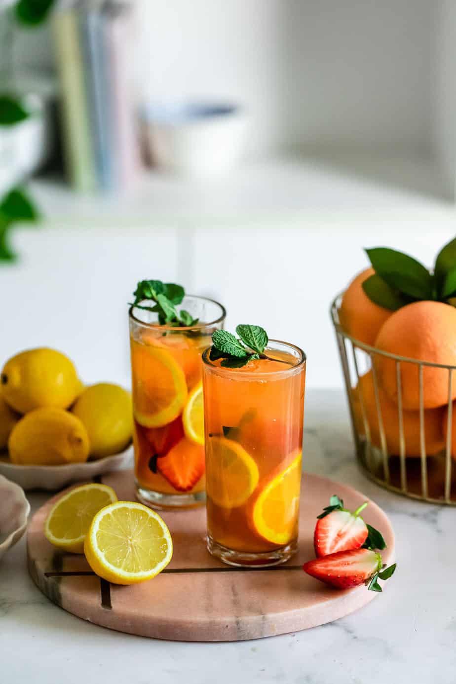 Two glasses filled with peach green tea and fresh fruit topped with mint.