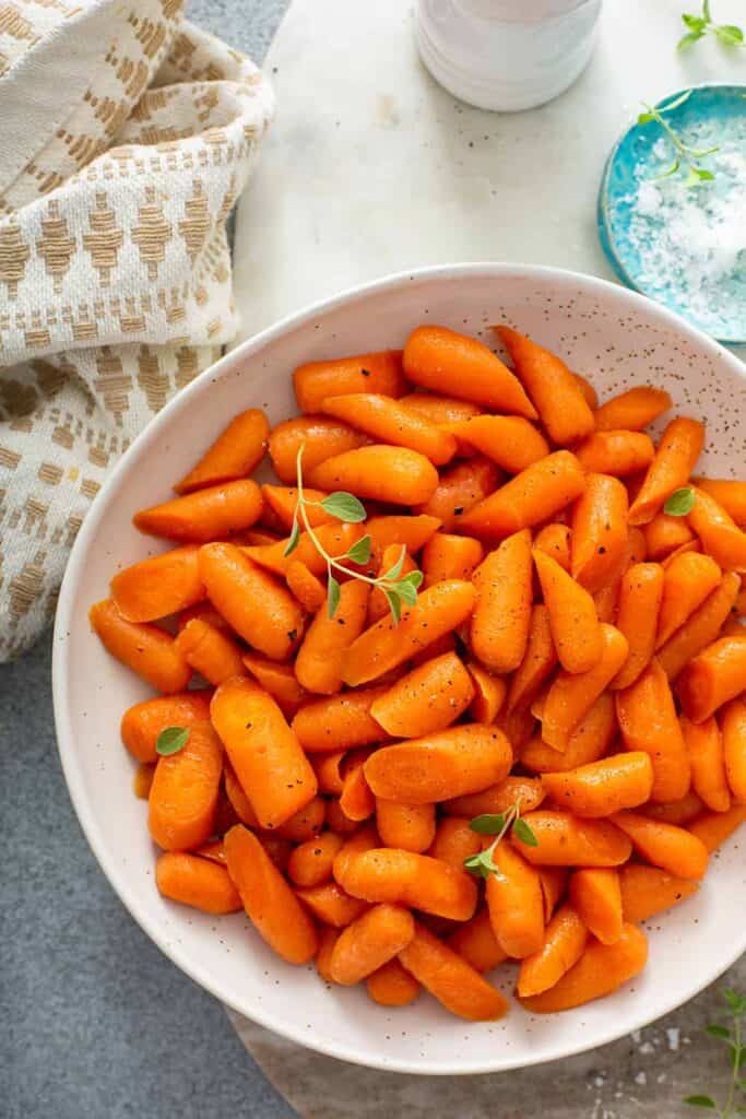 glazed carrots in large white bowl and small blue bowl with salt