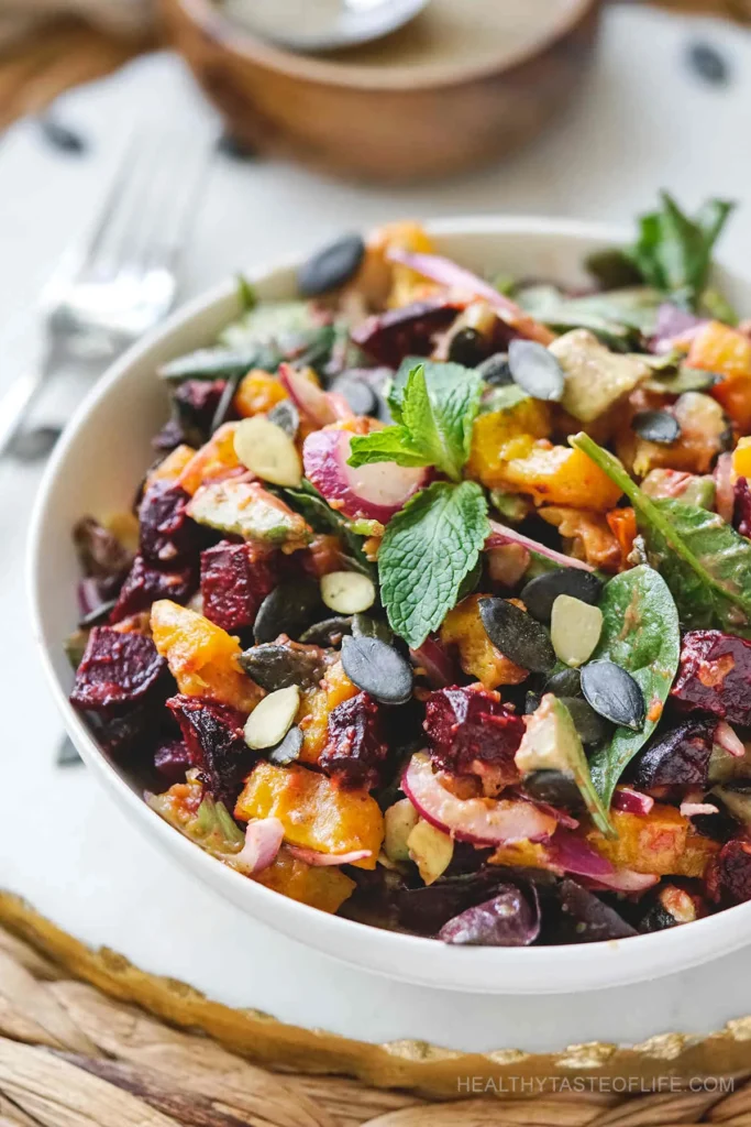 pumpkin and beet salad in white bowl with leafy greens