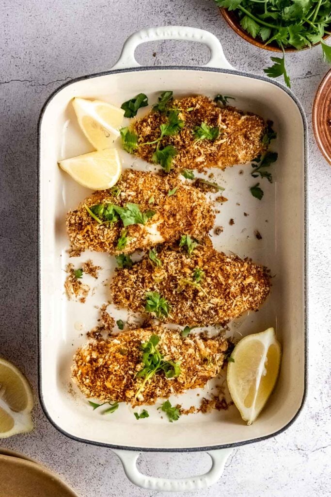white rectangular baking dish with four chicken breasts and lemon wedges