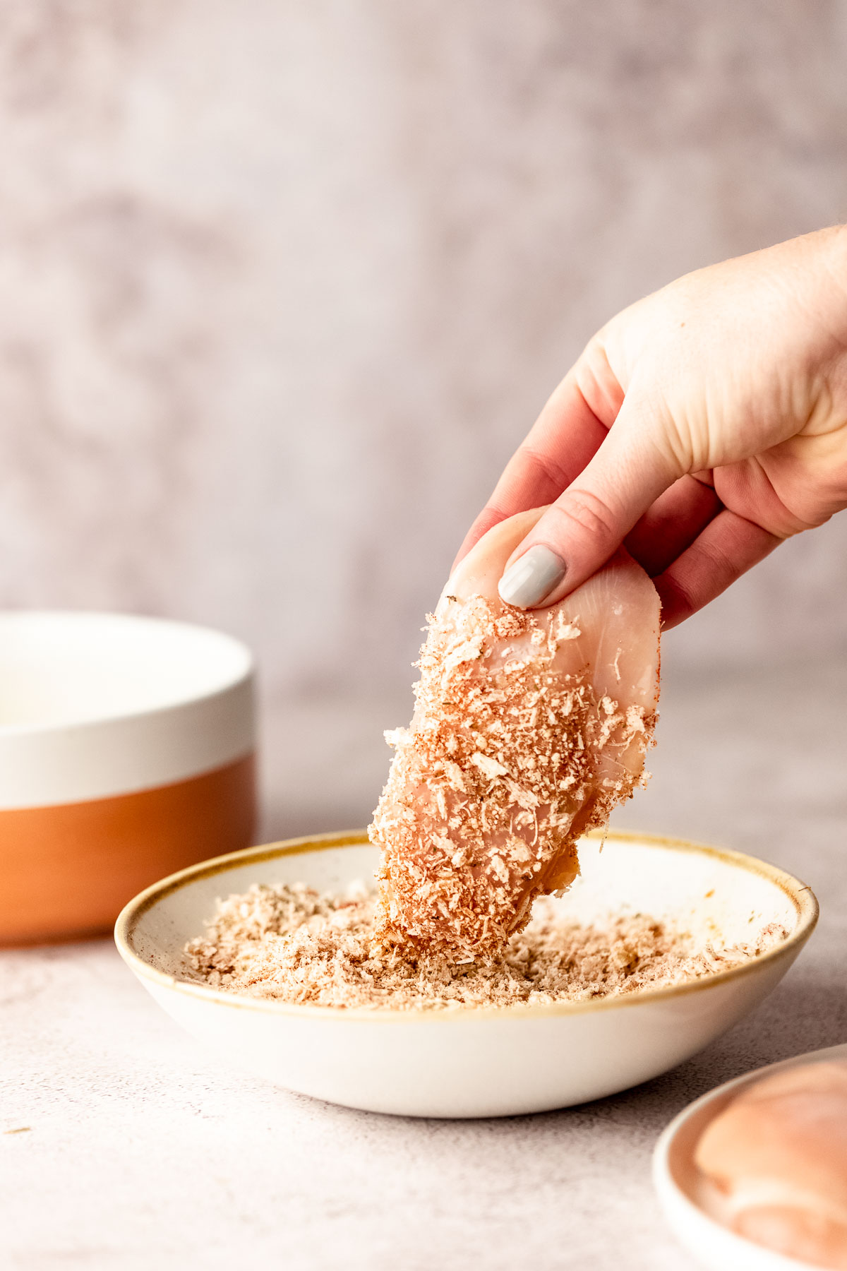 A chicken breast being coated with panko crumbs and parmesan