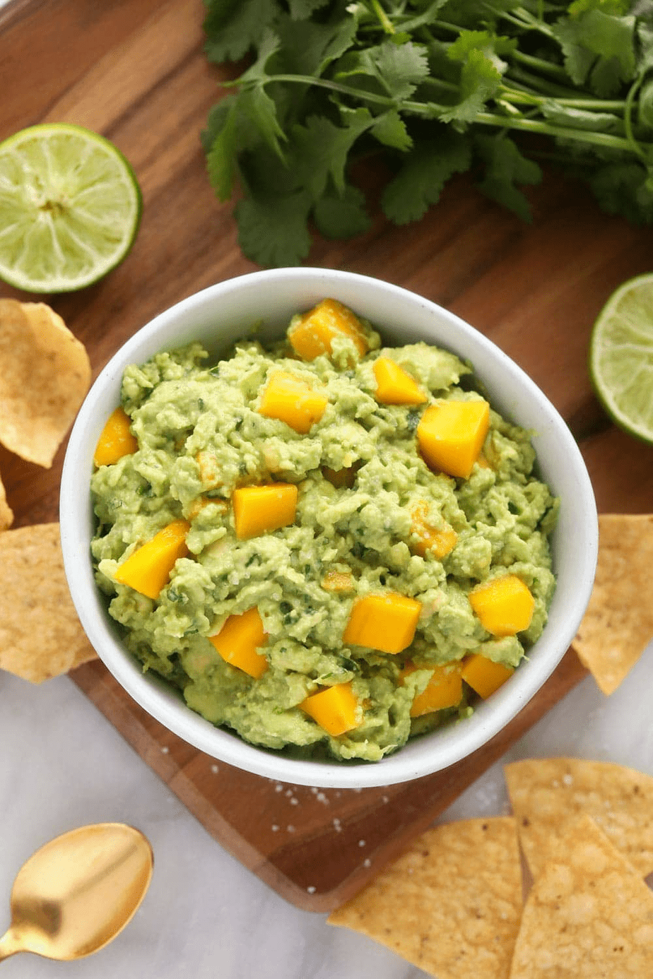 A white bowl of mango guacamole with tortilla chips.