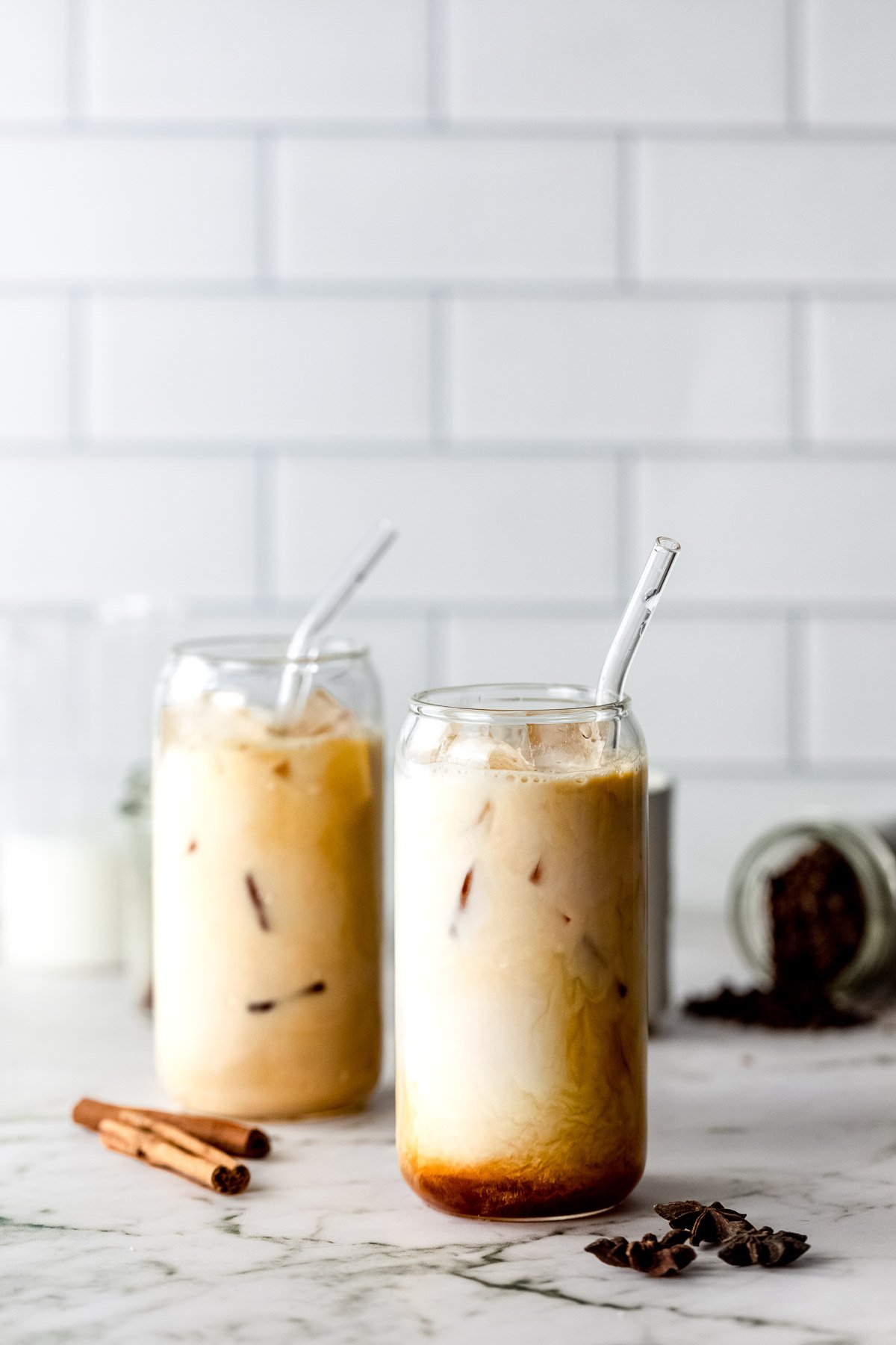Two glasses of dirty chai lattes with ice and served with glass straws.