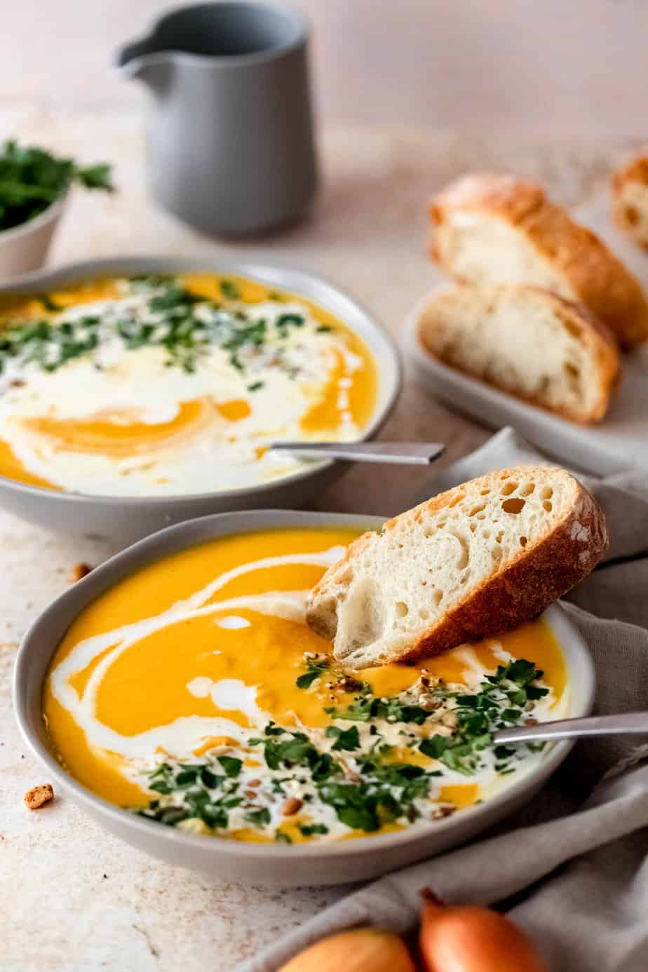 A bowl of soup served with fresh bread and garnished with cream and herbs.