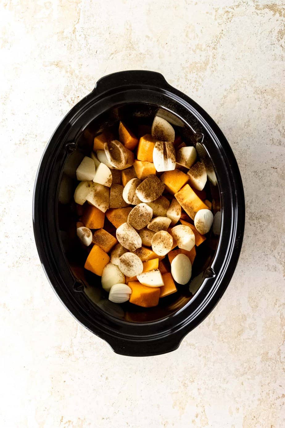 Chunks of pumpkin and potato in a slow cooker with spices and seasoning on top.