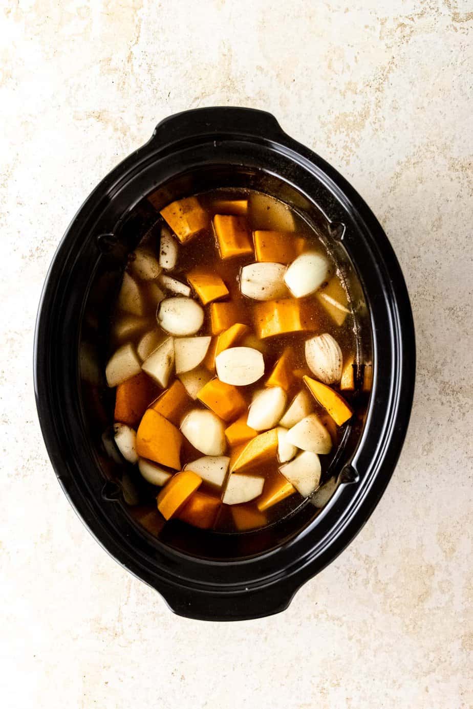 A slow cooker with vegetables and broth.