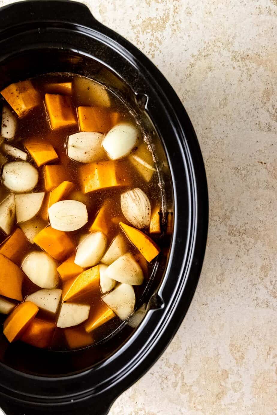 A slow cooker with vegetables and broth.