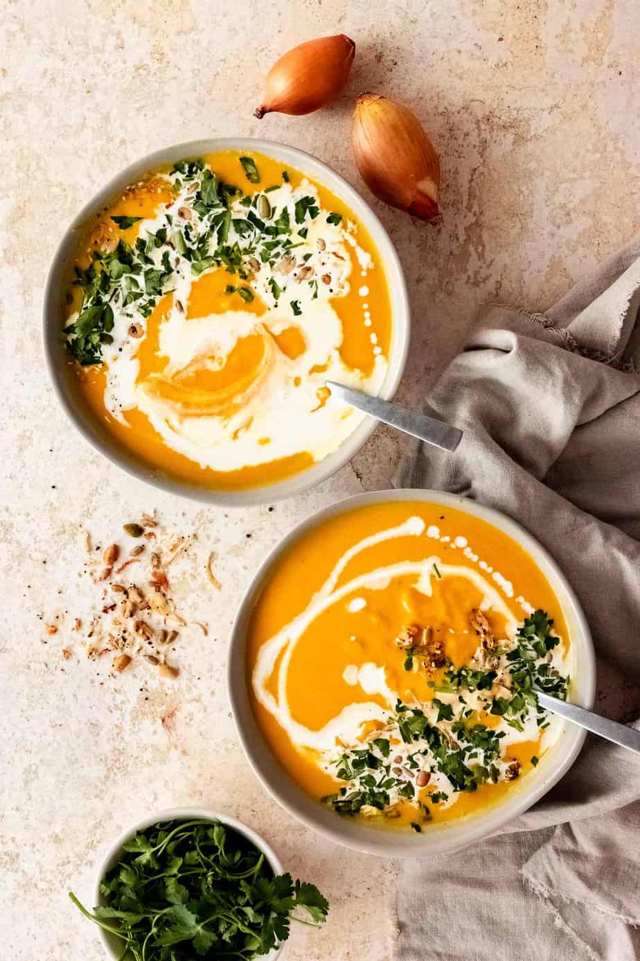 Two bowls of pumpkin soup with a drizzle of cream and fresh herbs on top.