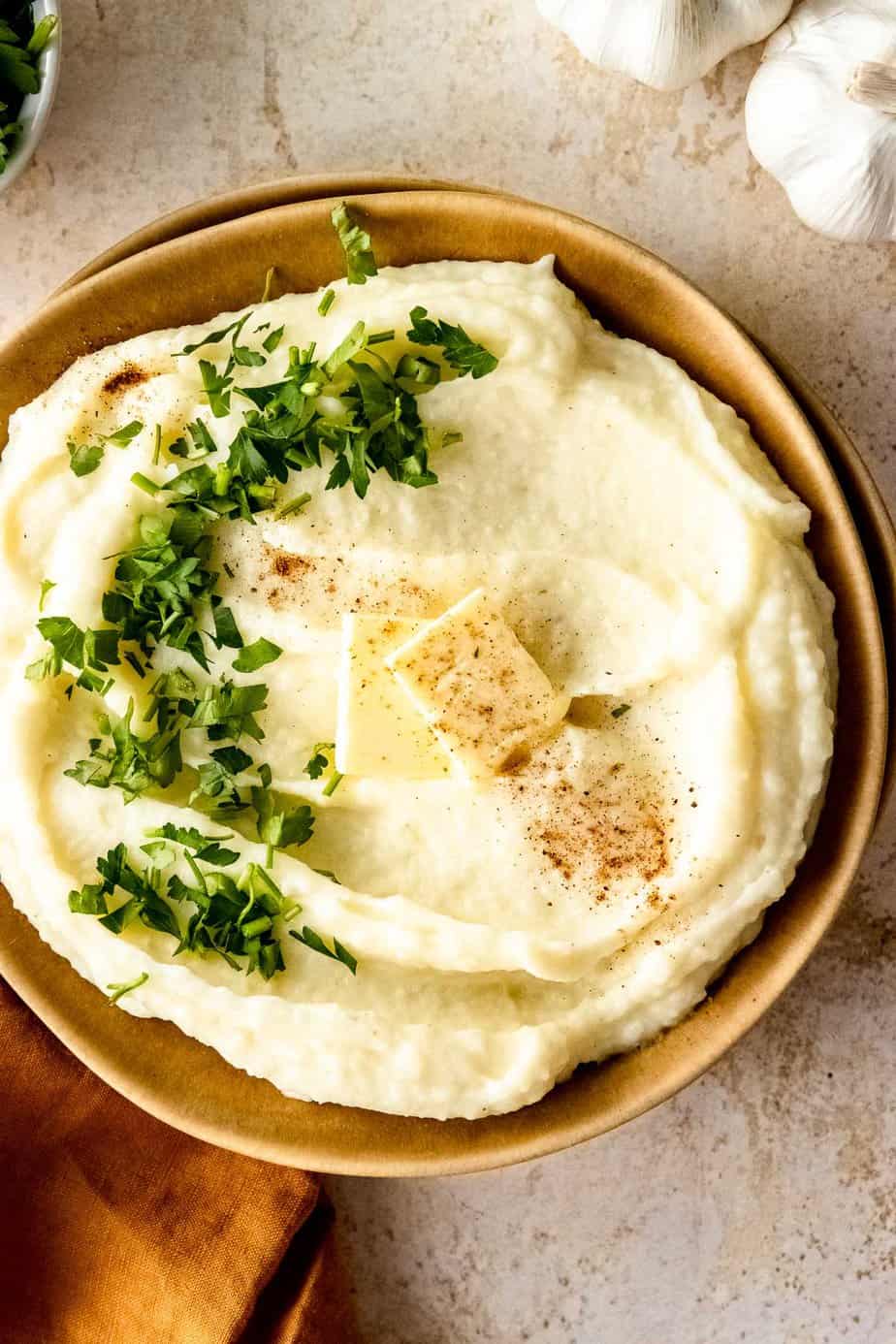 A close up of creamy mashed potatoes topped with fresh herbs, pepper, and butter.