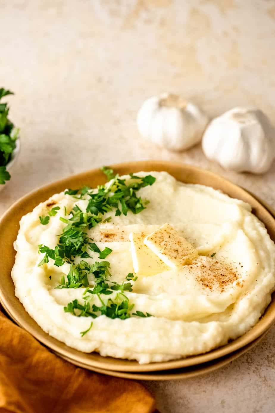 A bowl of mashed potatoes with butter, pepper, and fresh herbs.