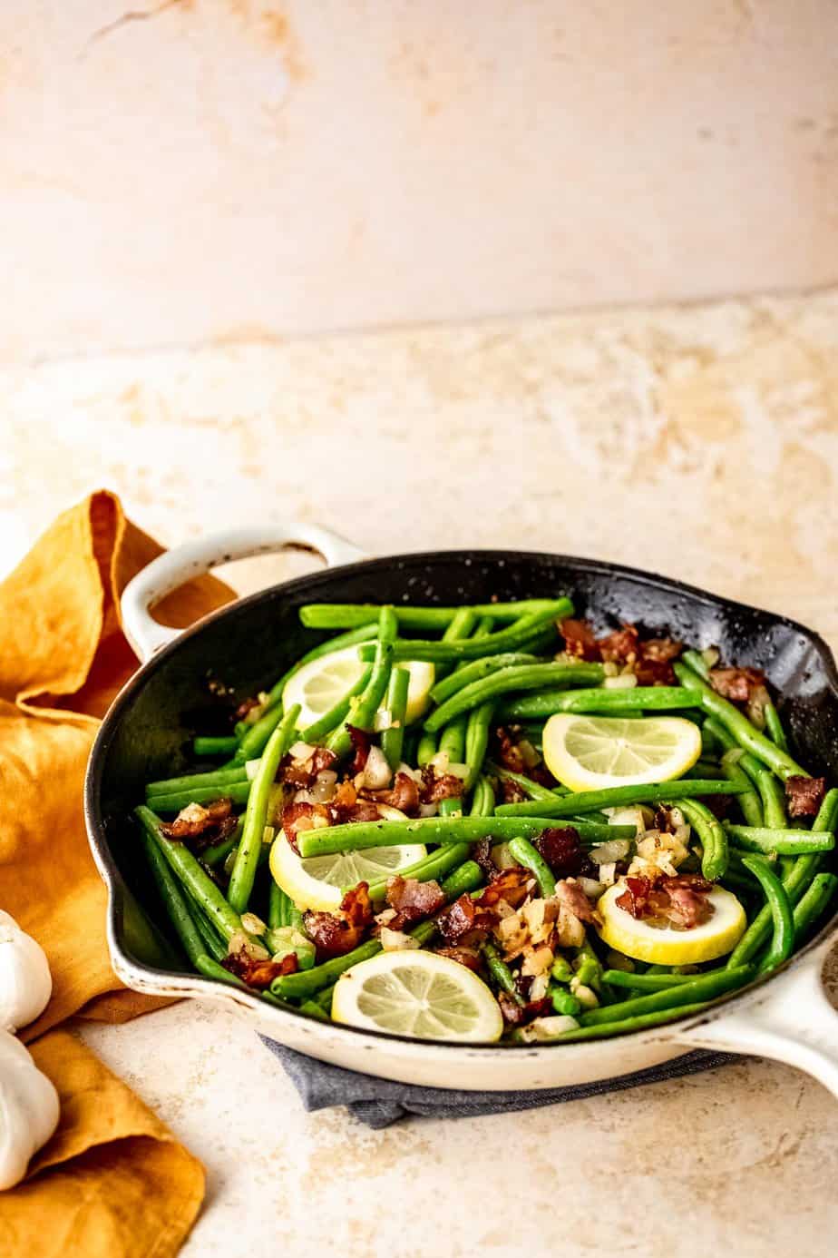 A skillet filled with crack green beans and garnished with fresh lemon.