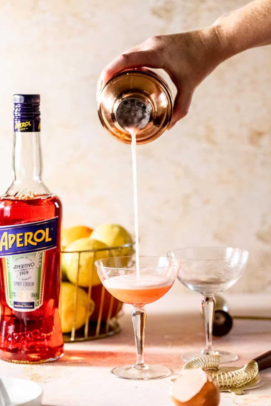 A cocktail shaker pouring a drink into a serving glass.