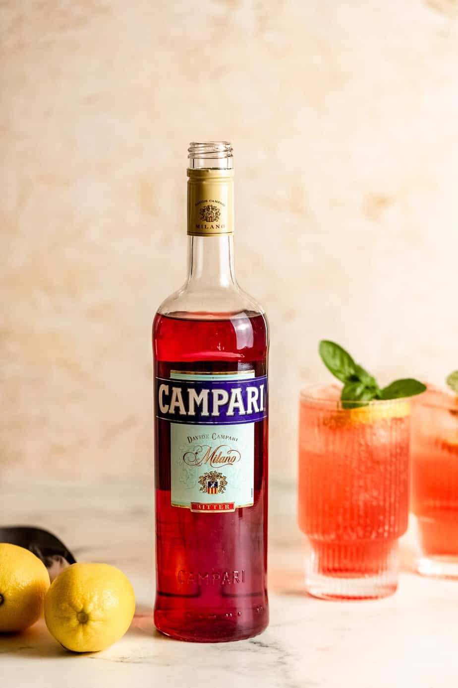 bottle of campari with fresh lemons and campari cocktails in background