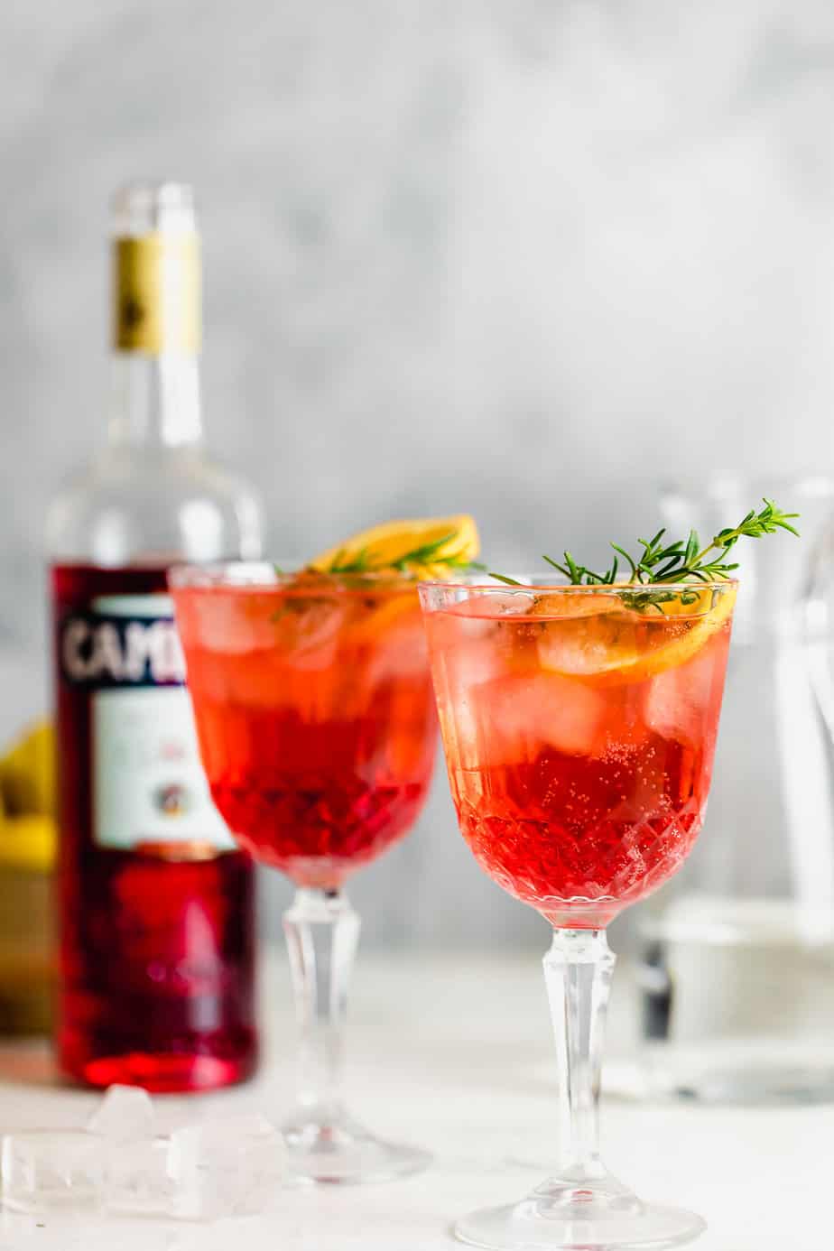 A classic Italian campari spritz cocktail on grey background with red campari bottle