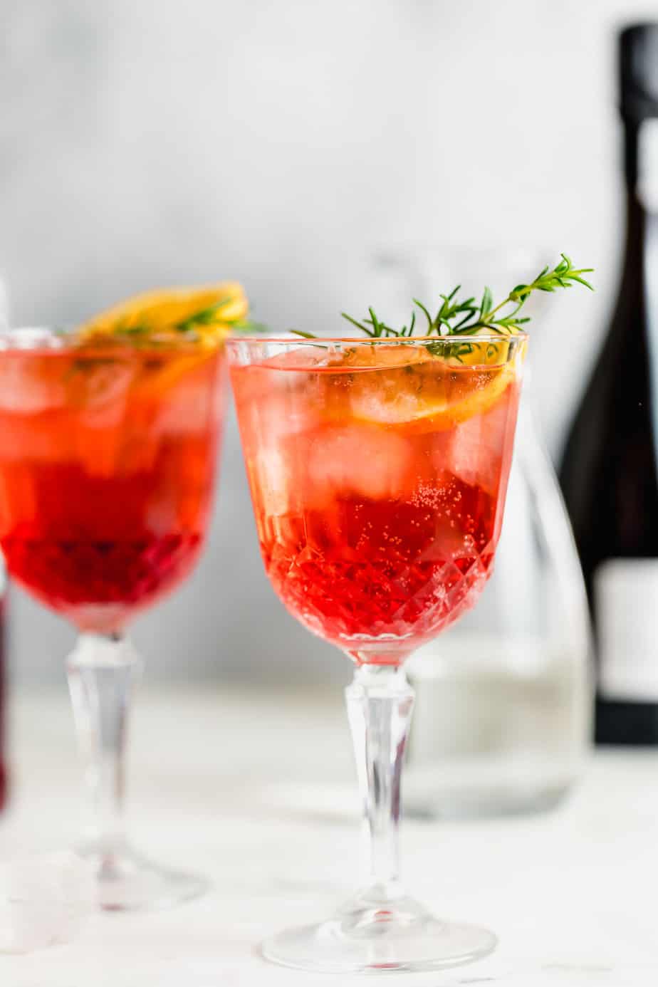 campari spritz with grey background topped with fresh herbs