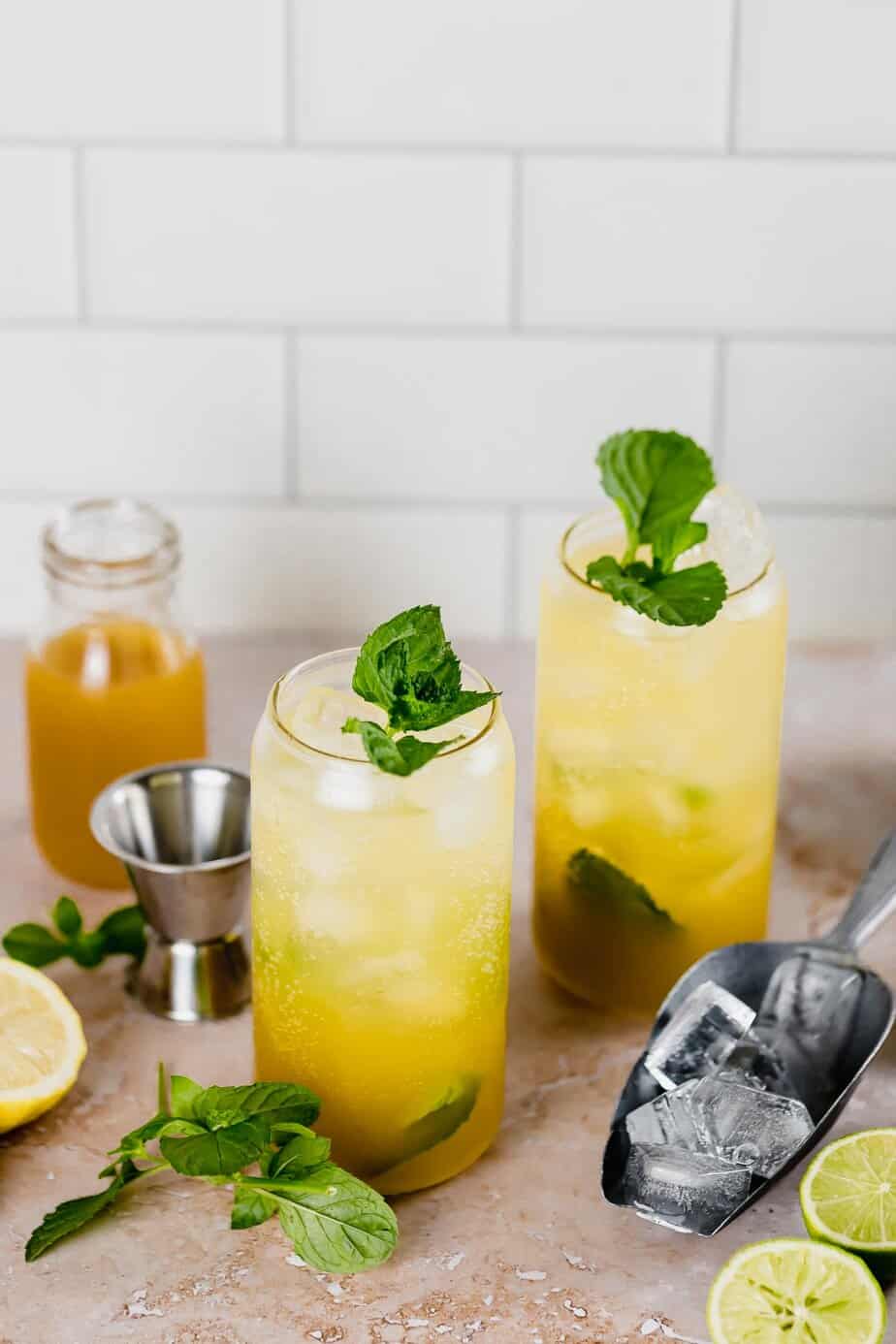 two glasses with mango mojito and mango nectar in small glass jar with fresh lemons and limes