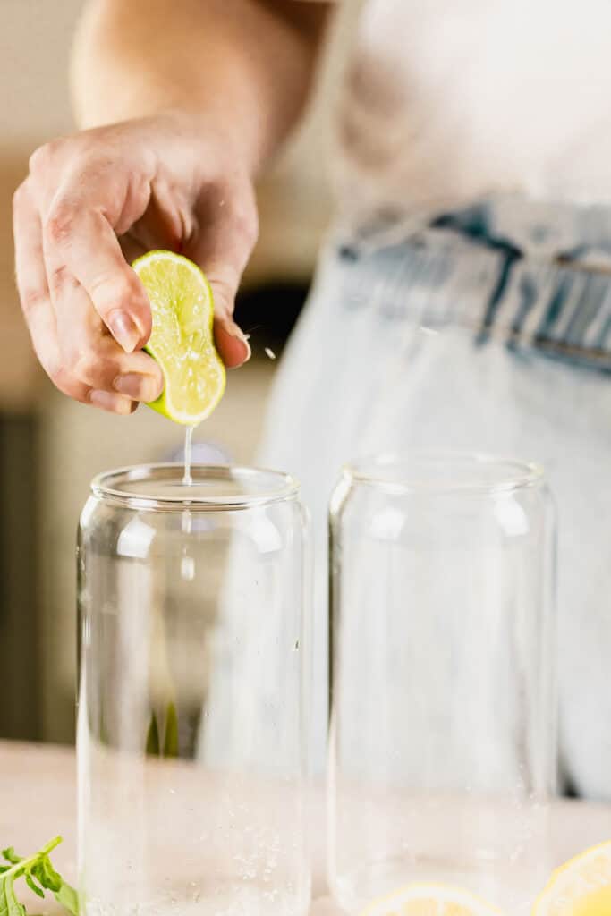 squeezing lime into glass with rum, sugar and lemon