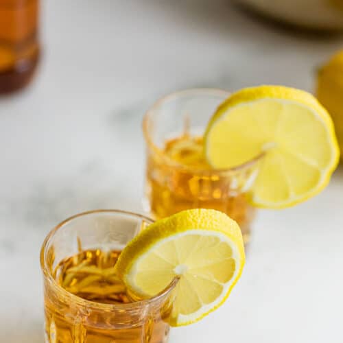 two whiskey shots with slices of lemon and bottle of whiskey in the background