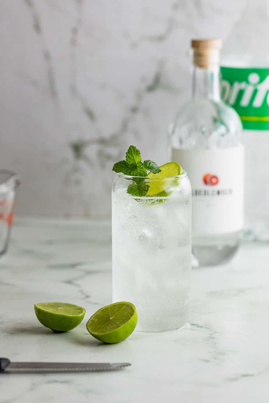 bottle of gin with glass of gin and sprite on marble