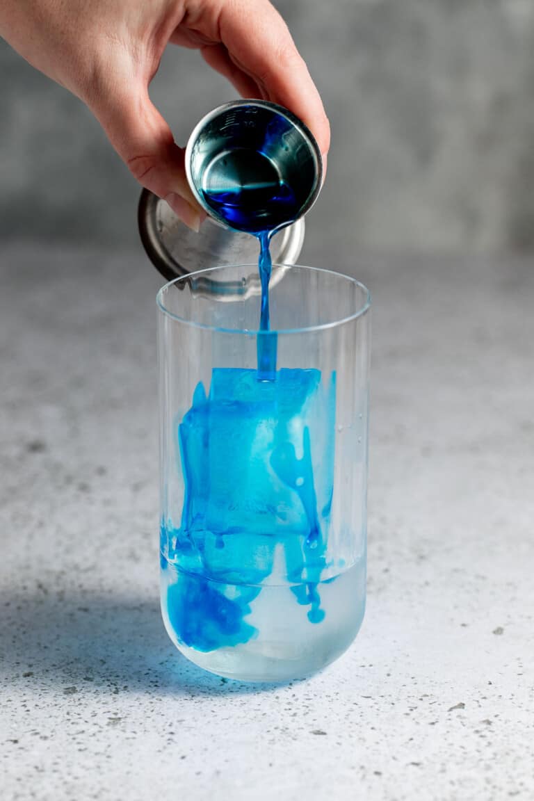pouring blue curacao into glass with ice