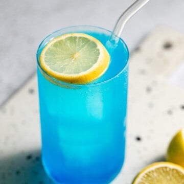 blue drink in tall glass with lemon slice as garnish and glass straw