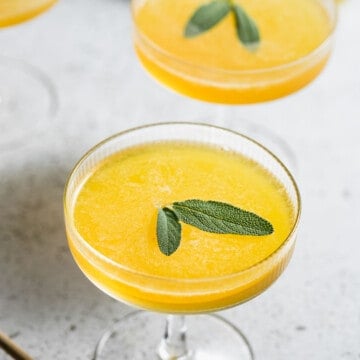 bee's knees cocktail in coupe glasses with sage leaves