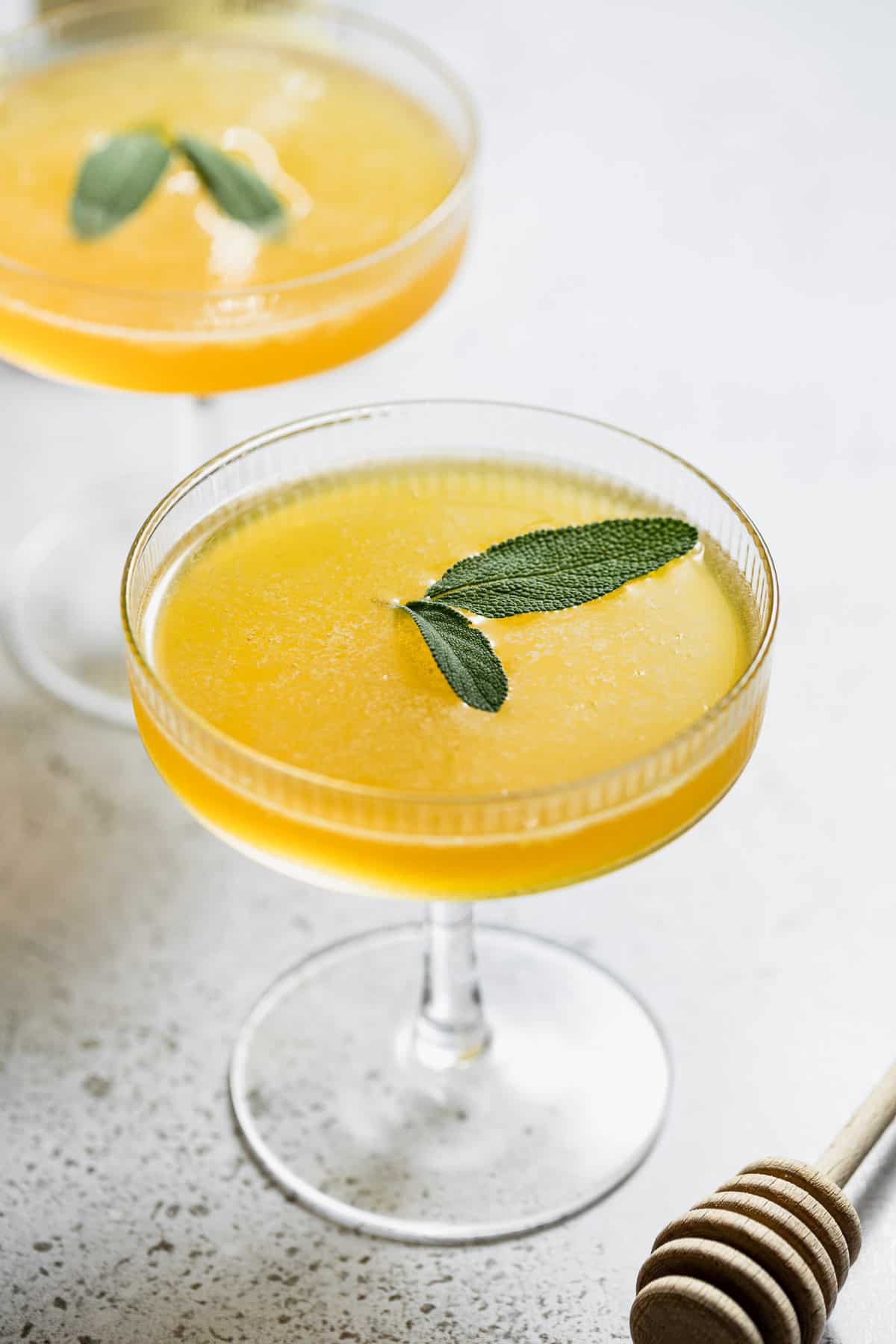 cocktail with honey and lemon juice in coupe glasses garnished with sage