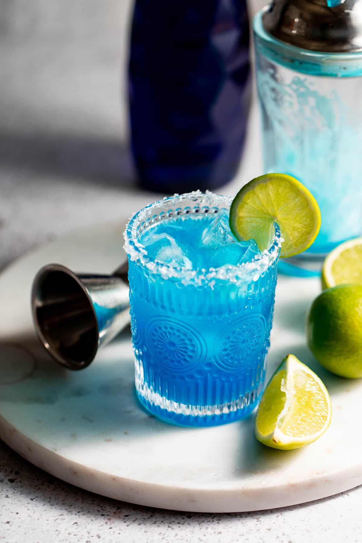 blue margarita on marble background with jigger and fresh limes