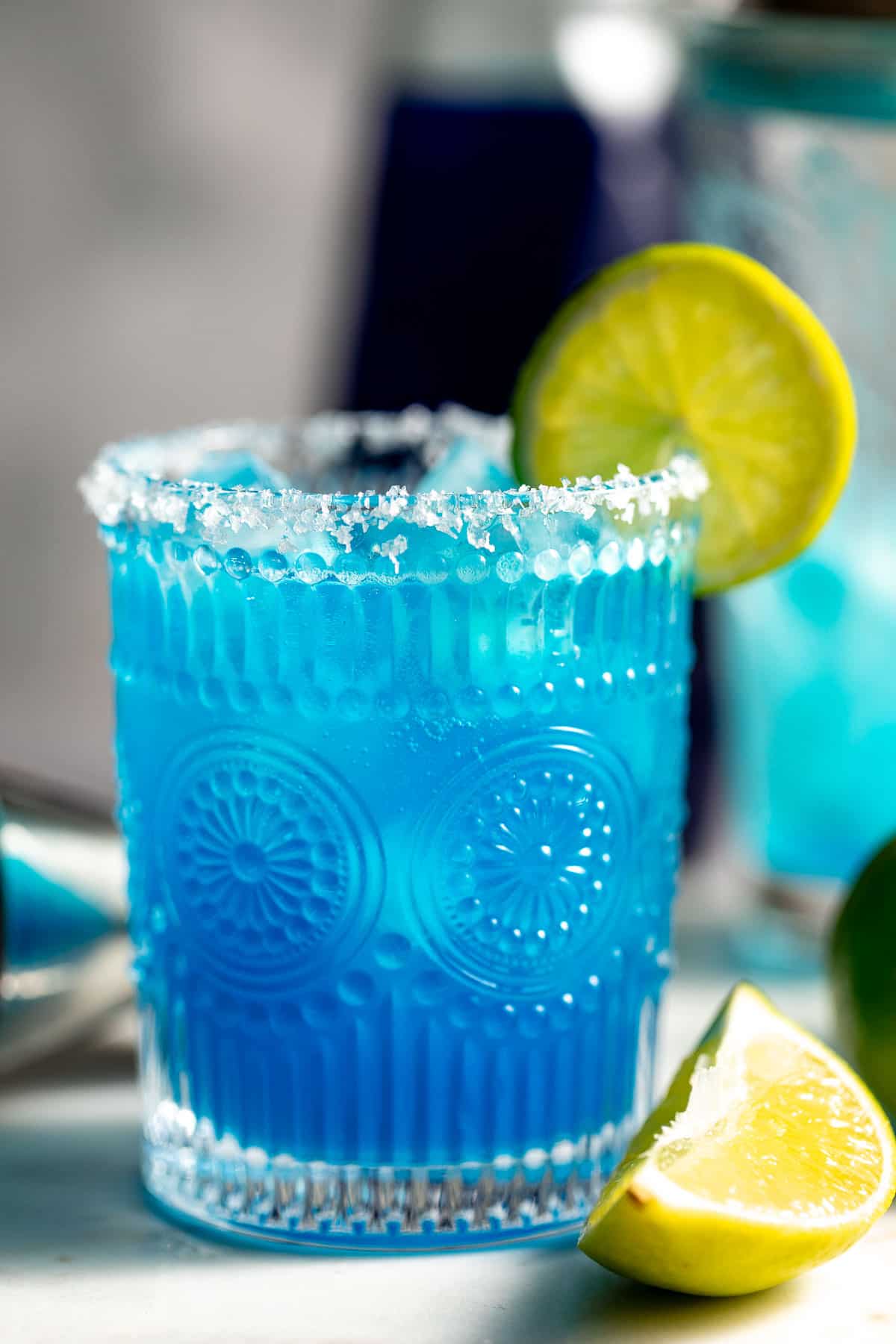 glass with blue margarita garnished with salt and lime