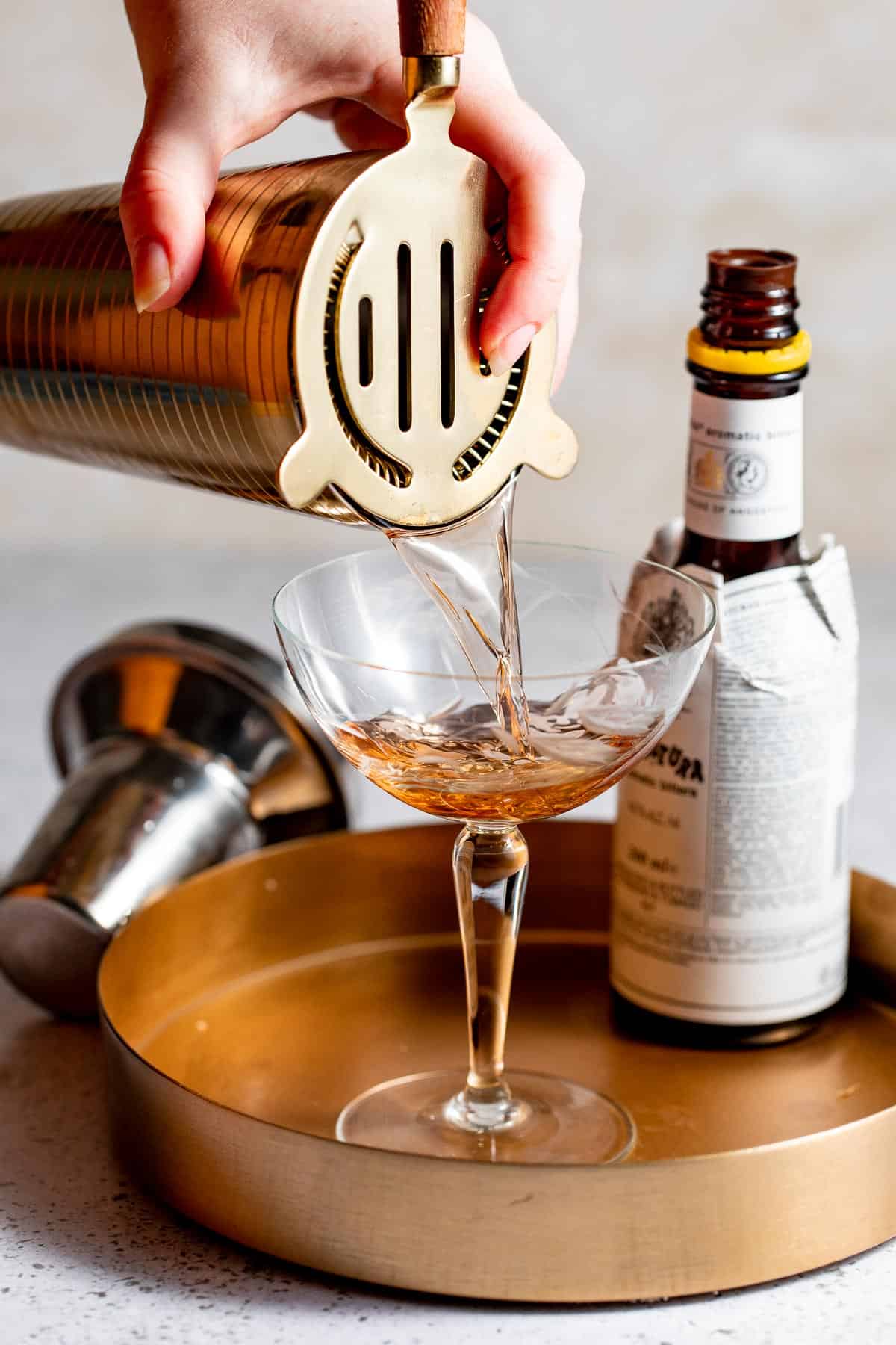 A brandy manhattan cocktail being poured into a serving glass.
