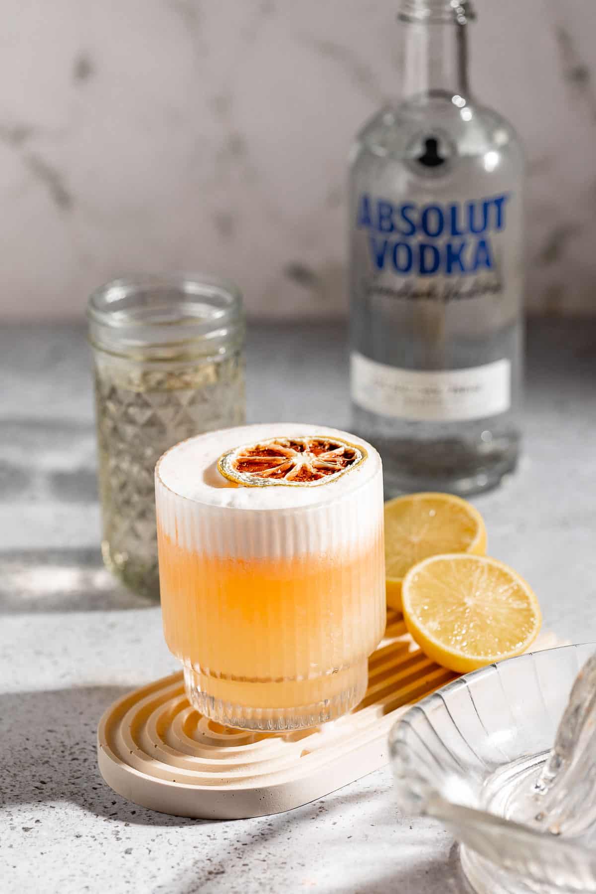 vodka sour on grey background with bottle of absolut vodka and simple syrup in jar