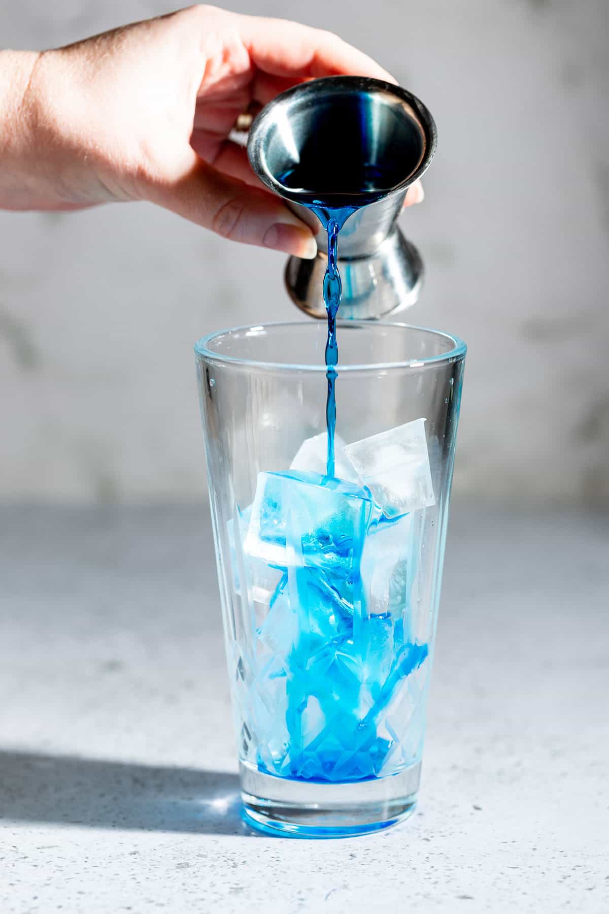 Blue curacao pouring into a cocktail shaker filled with ice.