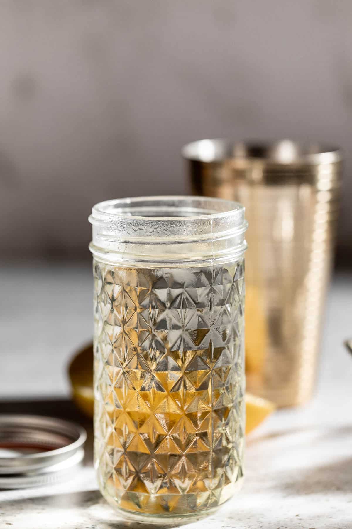 simple syrup in glass jar with cocktail shaker in the background