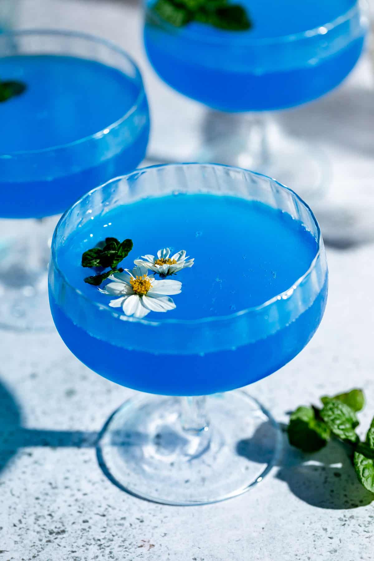 three coupe glasses with blue cocktail