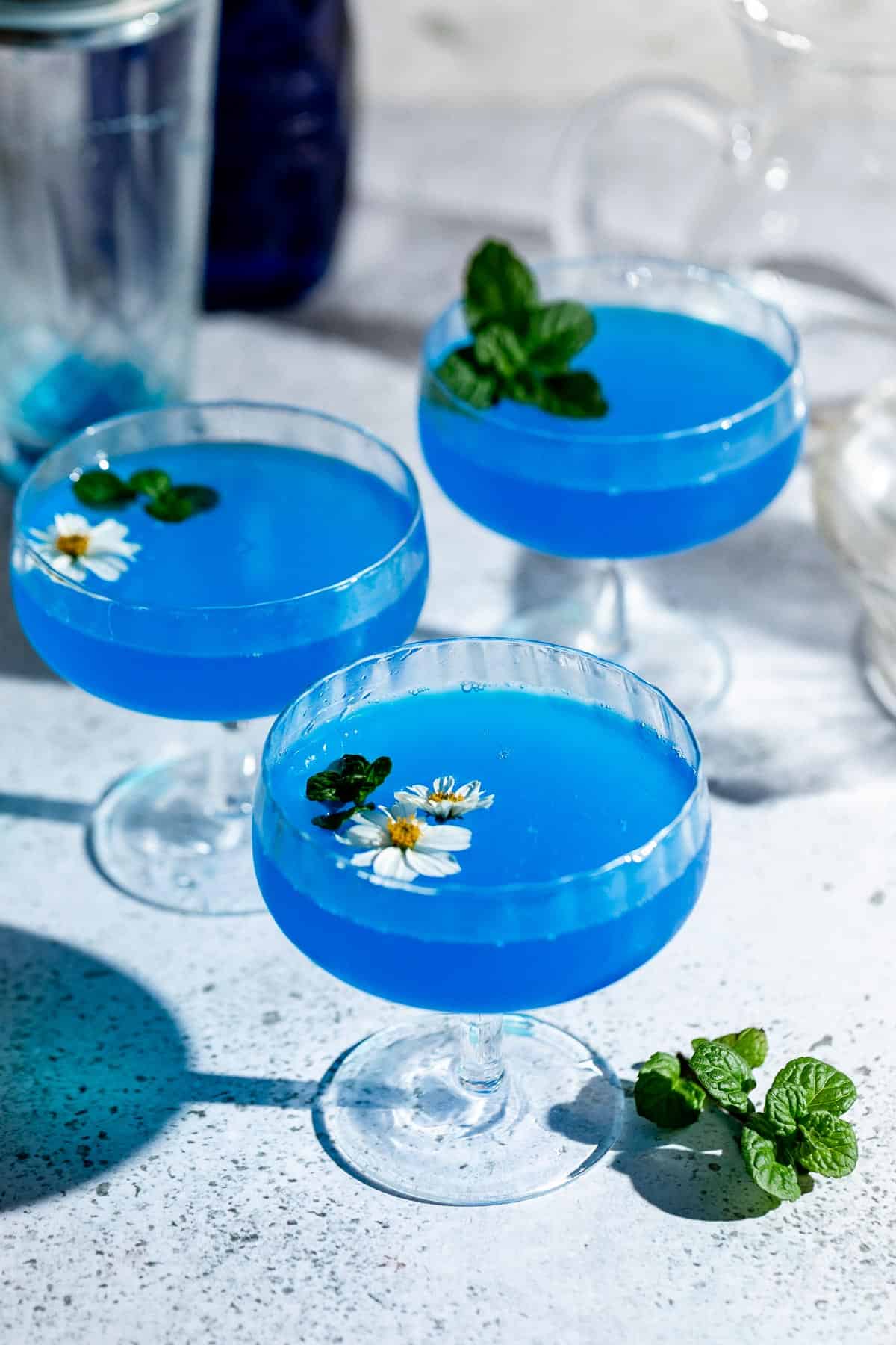 three coupe glasses on gray background filled with blue cocktail