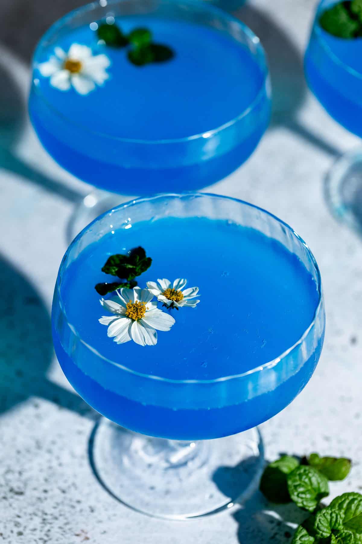 blue lagoon cocktail in coupe glasses garnished with white flowers