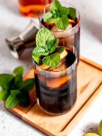 Jack and coke in two tall glasses garnished with fresh mint