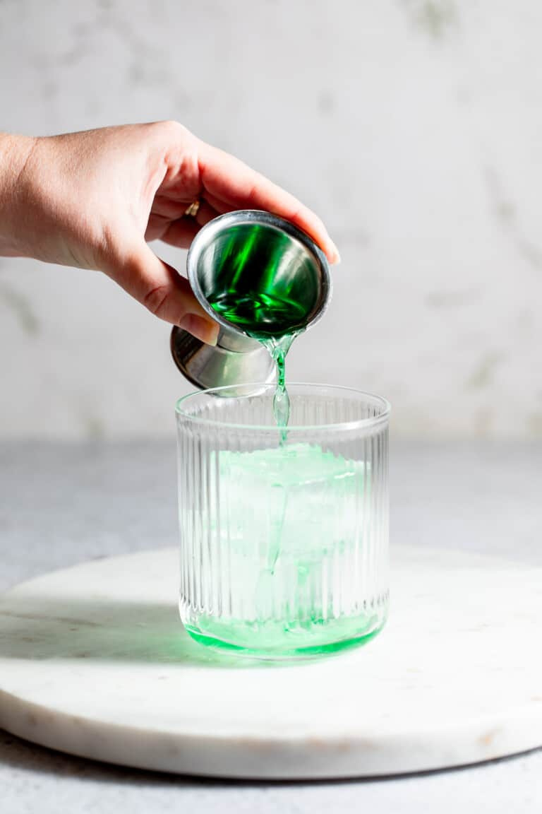 pouring midori into glass over ice