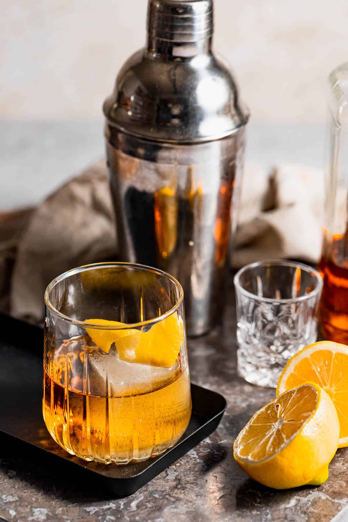 A cocktail garnished with orange zest on a black serving tray.