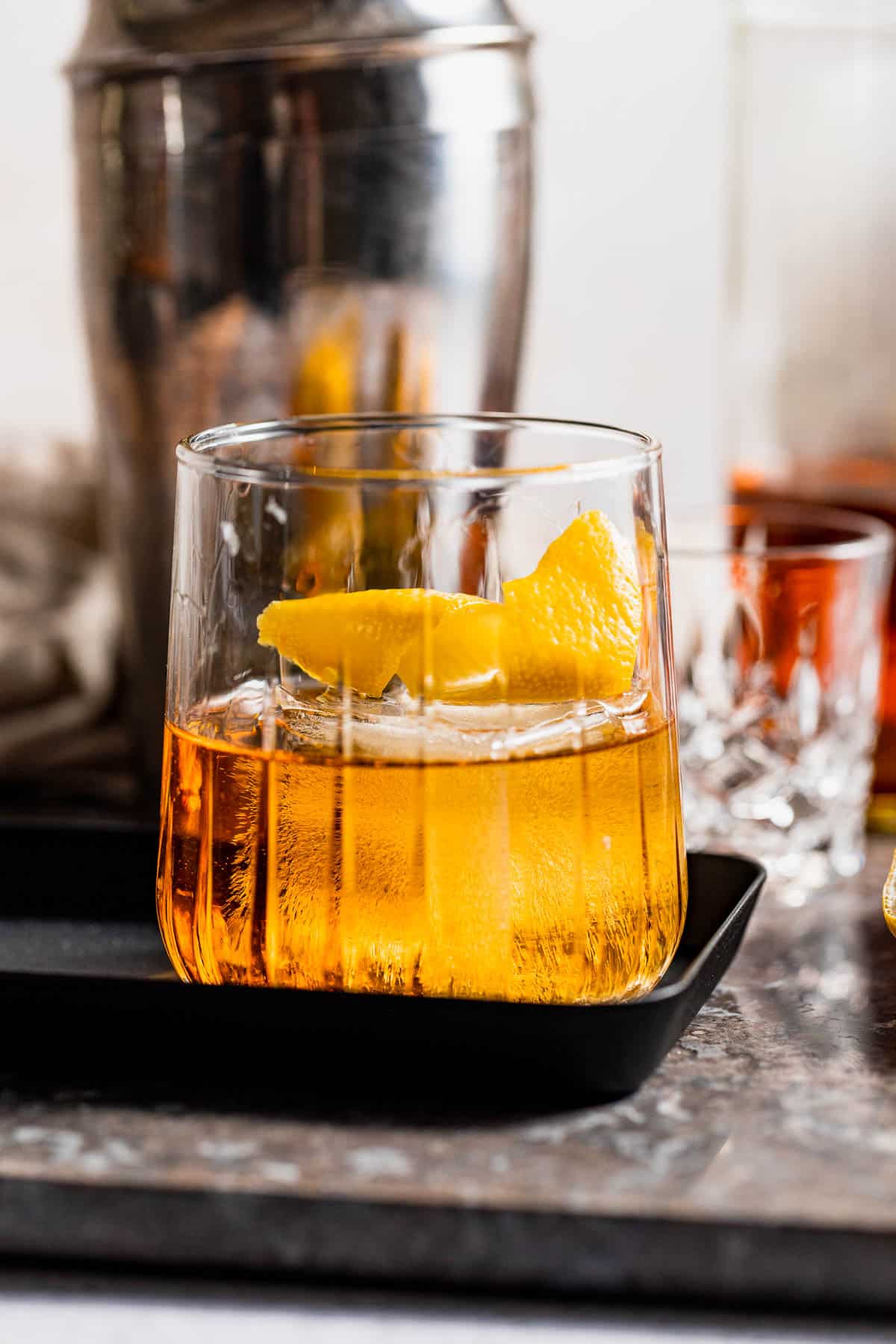 A godmother drink garnished with orange zest on a black serving tray.