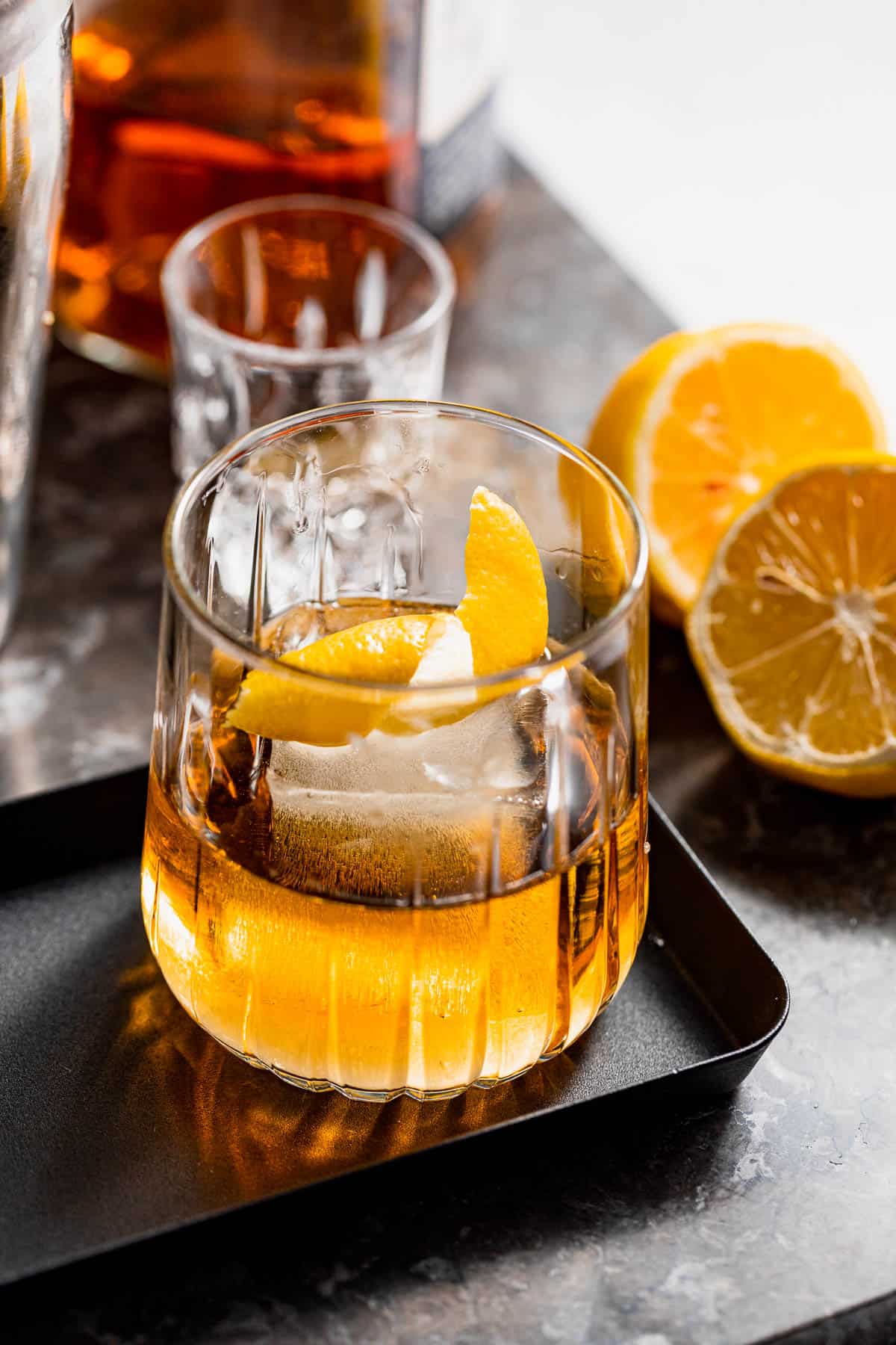 A godmother drink garnished with orange zest on a black serving tray.