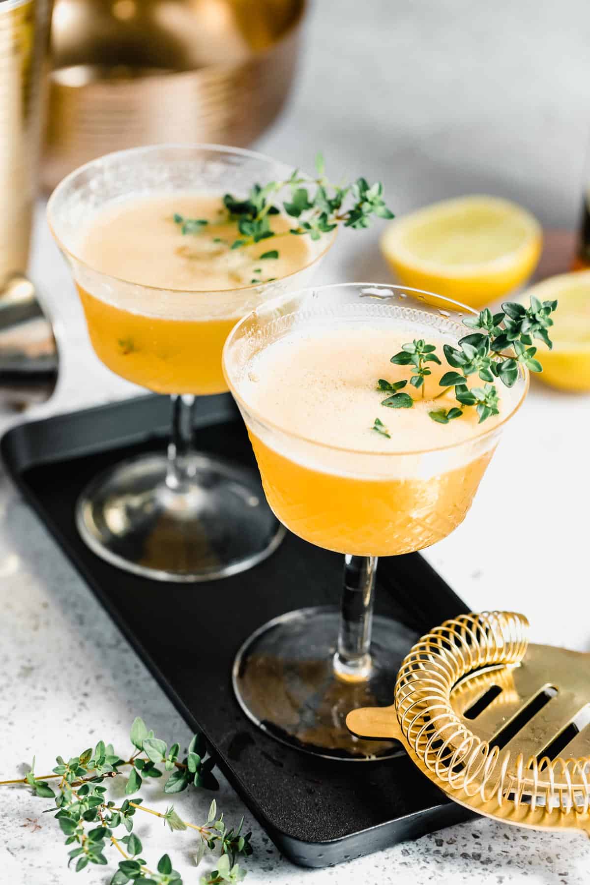 Two upscale drinks on a black serving tray garnished with fresh thyme.