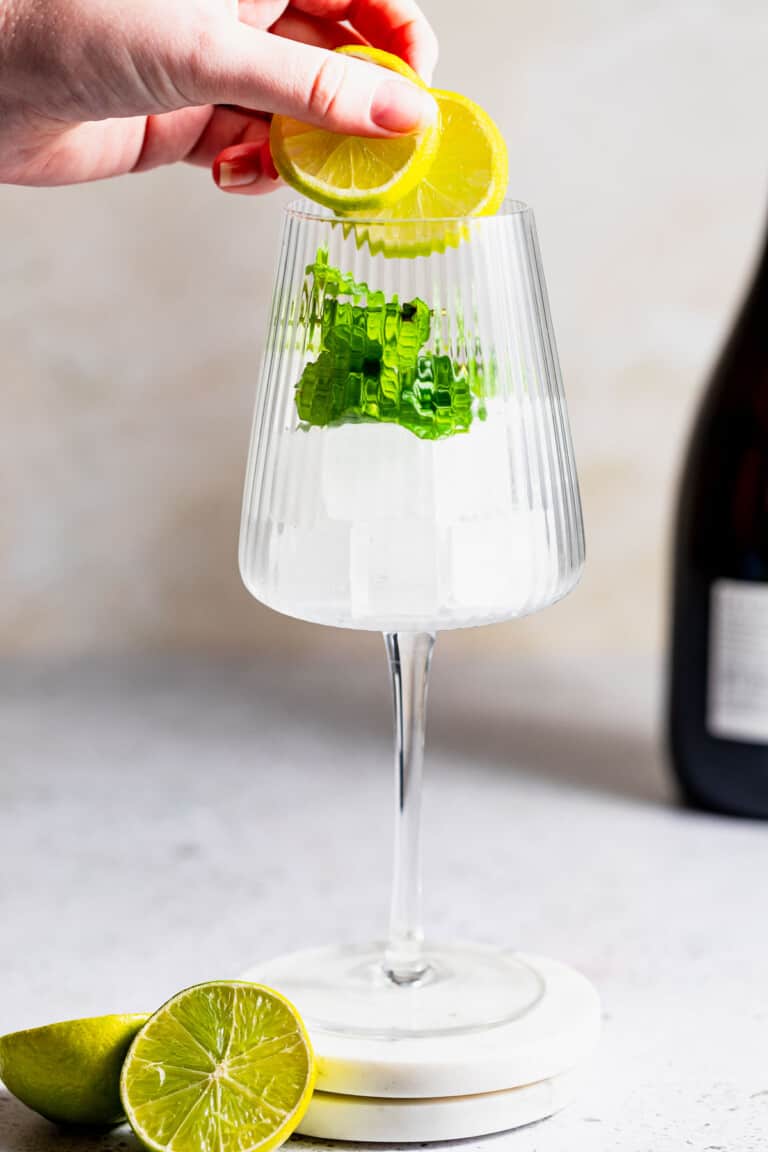 A person adding lime slices to a glass filled with ice and mint