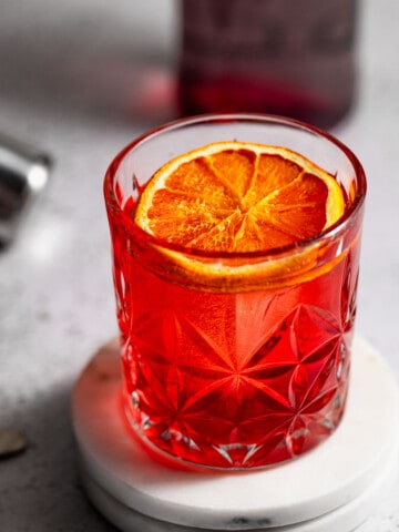 mezcal negroni on two marble coasters and topped with dried orange slice