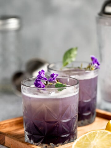 purple rain drink on wooden tray topped with fresh flowers