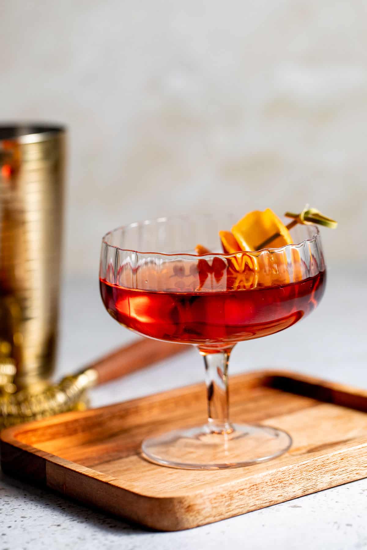 wooden tray topped with coupe glass filled with an upscale drink.