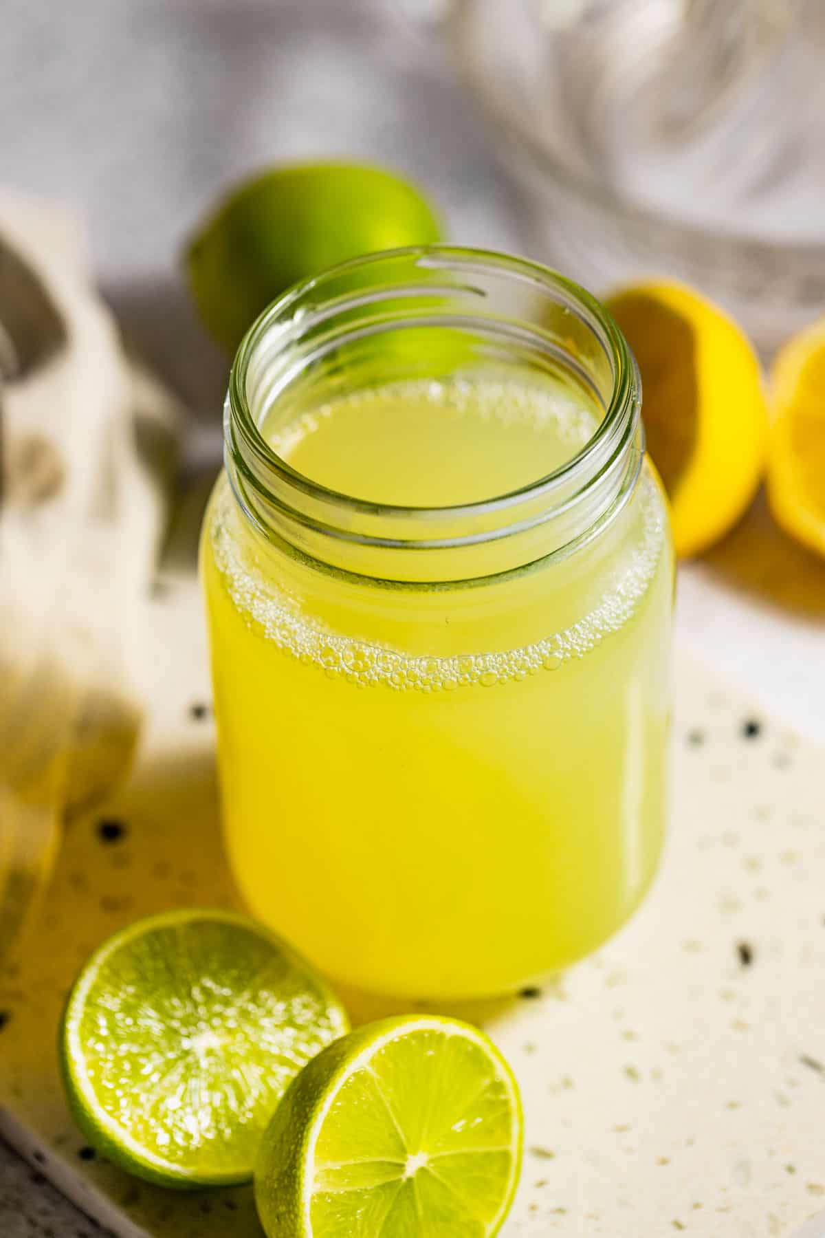 sour mix for cocktails in a mason jar with halved lemons and limes
